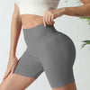 A woman wearing high-waisted gray yoga shorts and a white sports bra, shown from the back.