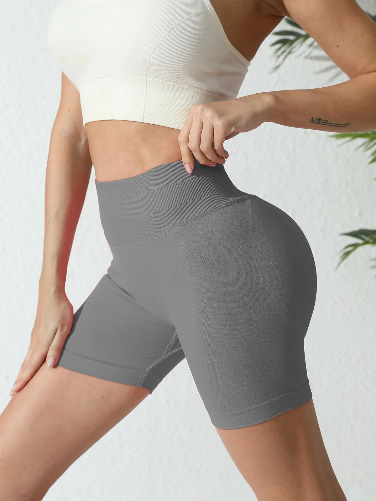A woman wearing high-waisted gray yoga shorts and a white sports bra, shown from the back.