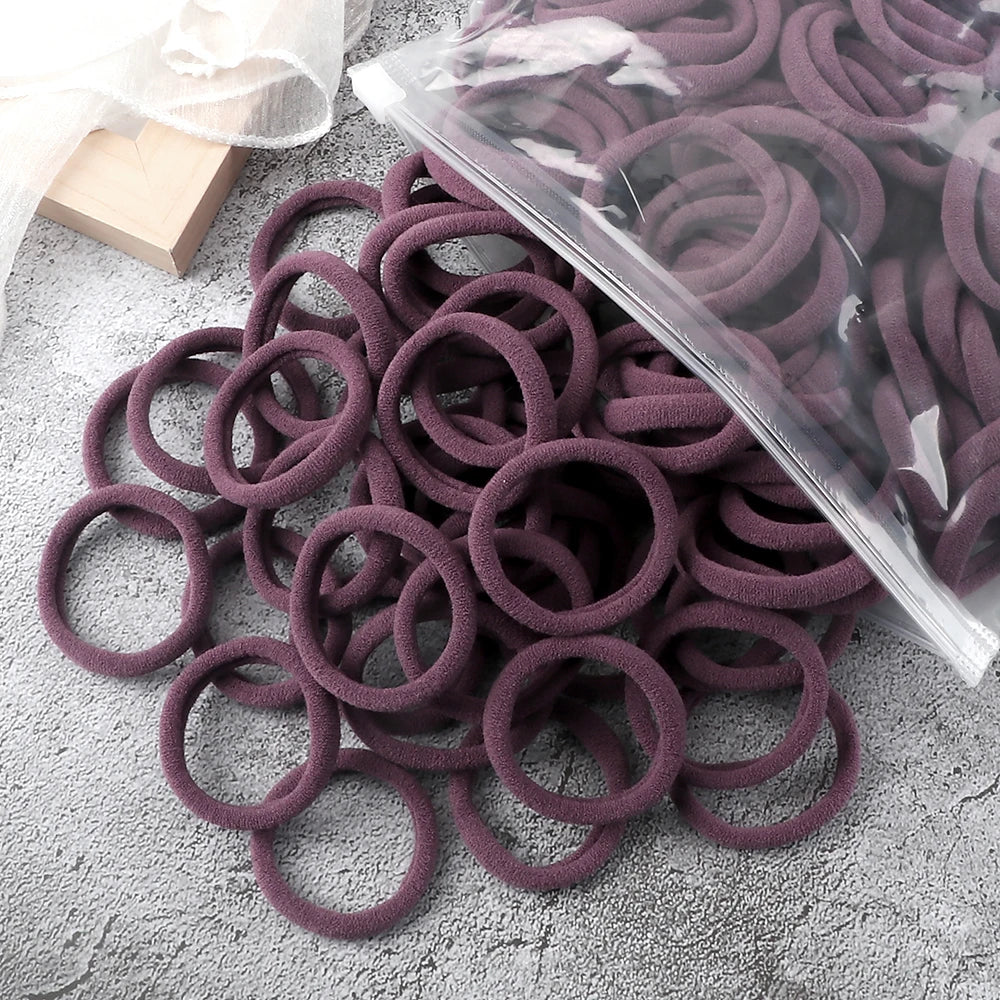 A pile of 50 pieces of mixed color elastic hair bands in shades of purple and mauve on a gray surface.