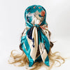 A teal and cream satin square scarf tied around a woman's hair, featuring a floral and abstract pattern.