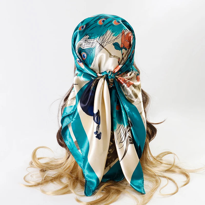 A teal and cream satin square scarf tied around a woman's hair, featuring a floral and abstract pattern.