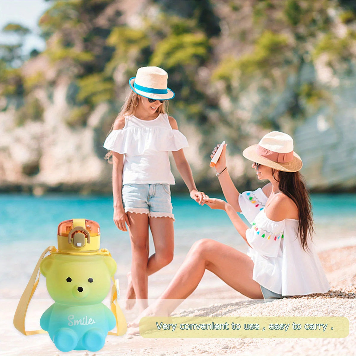 A woman is holding a portable bear water bottle with a straw and strap on a beach.