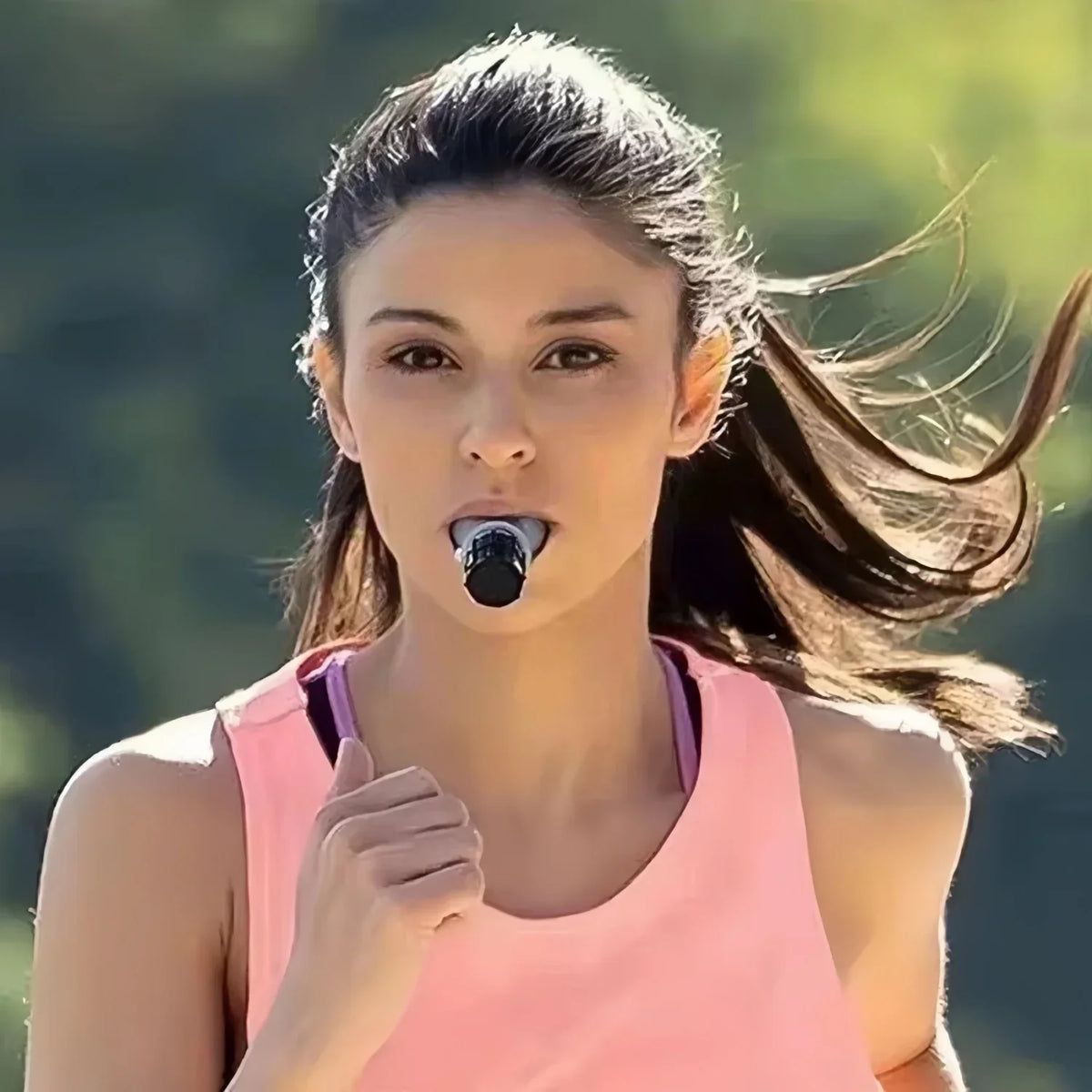 A young woman with dark hair is shown outdoors, holding a silicone breathing trainer near her mouth.