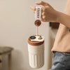 A hand holds a white insulated thermos bottle with a coffee tag, showing the smart display top.