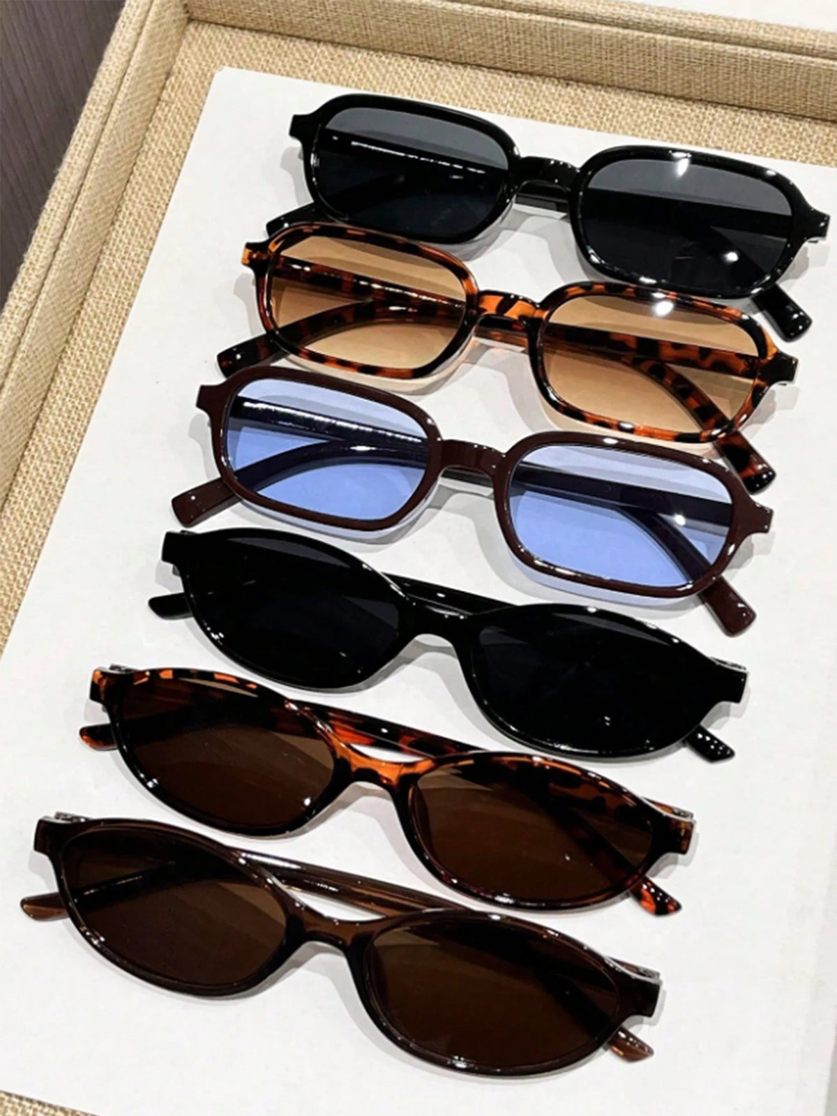 A set of eight retro fashion sunglasses in various brown, tortoiseshell, and blue shades displayed on a white card.