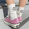 A pair of pink Converse shoes with white laces and white knitted socks featuring embroidered text