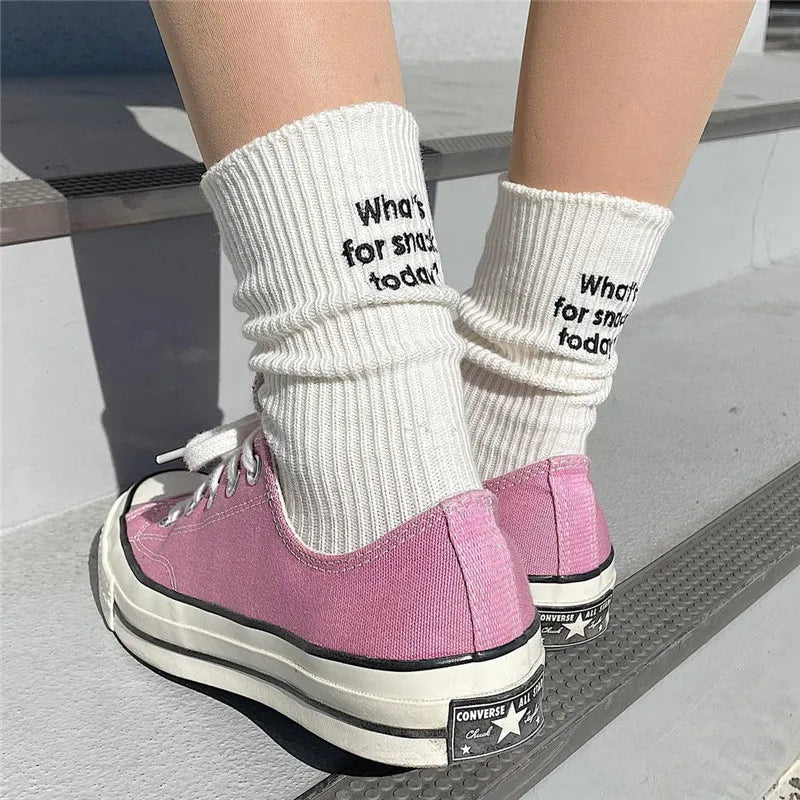 A pair of pink Converse shoes with white laces and white knitted socks featuring embroidered text