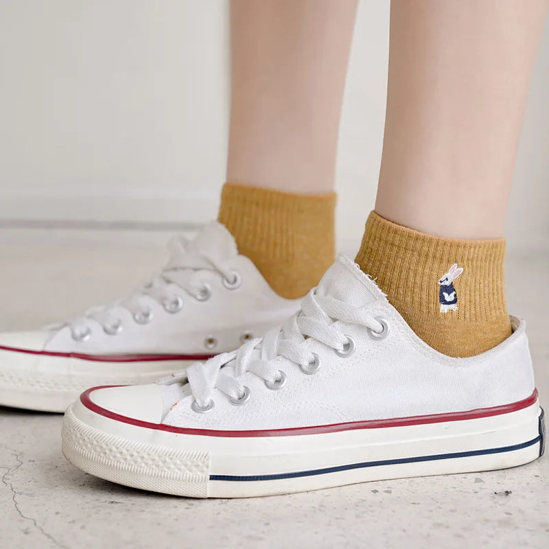 White embroidered canvas sneakers worn by a person with mustard yellow socks.