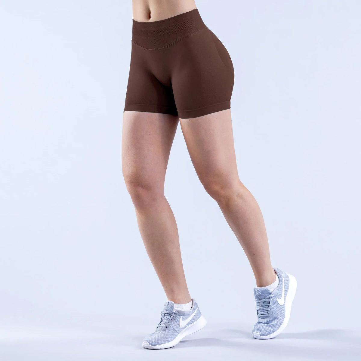 A person is wearing brown seamless high-waisted yoga shorts and light gray athletic shoes.