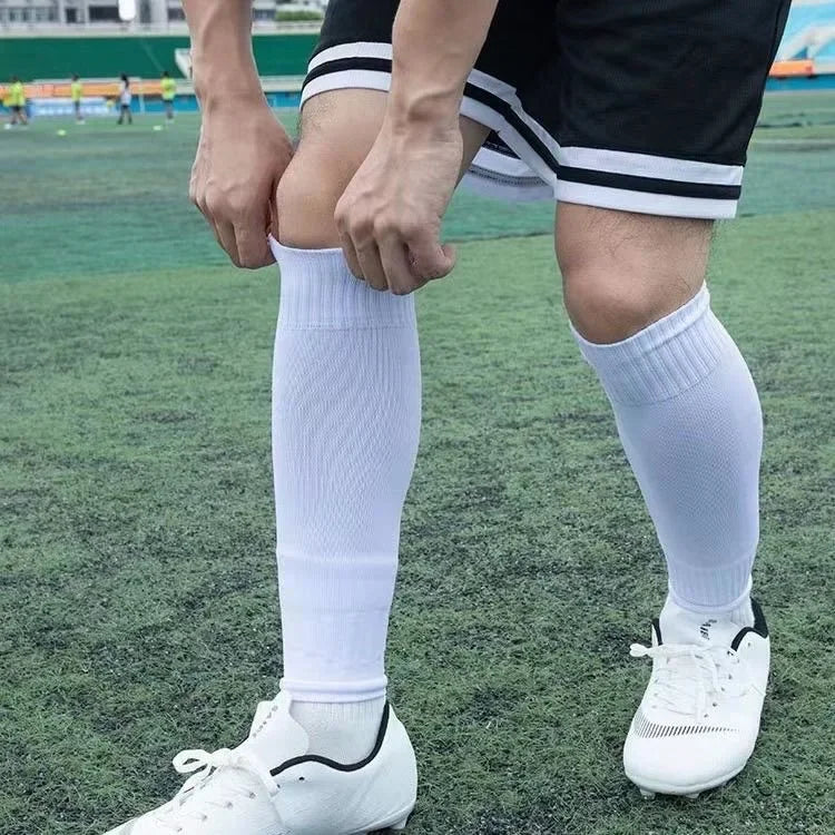Close-up of a person wearing white compression sports socks and white football cleats on a green field.