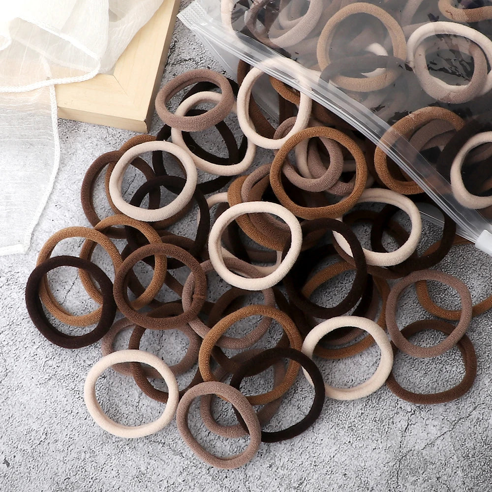 A pile of 50 pieces of mixed color elastic hair bands, including brown and beige tones, are displayed on a gray surface.