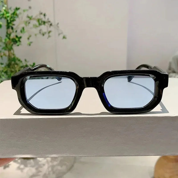 Black rectangular sunglasses with blue mirrored lenses resting on a white surface.