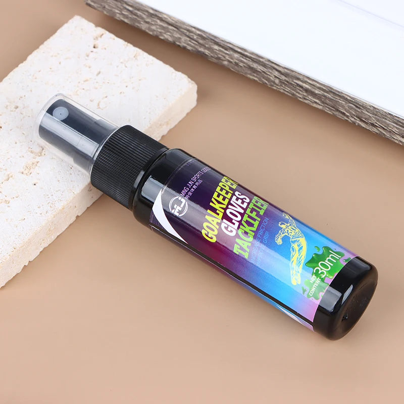 A bottle of Goalkeeper Gloves Tactifier spray with a black pump dispenser resting on a beige surface next to a white block.