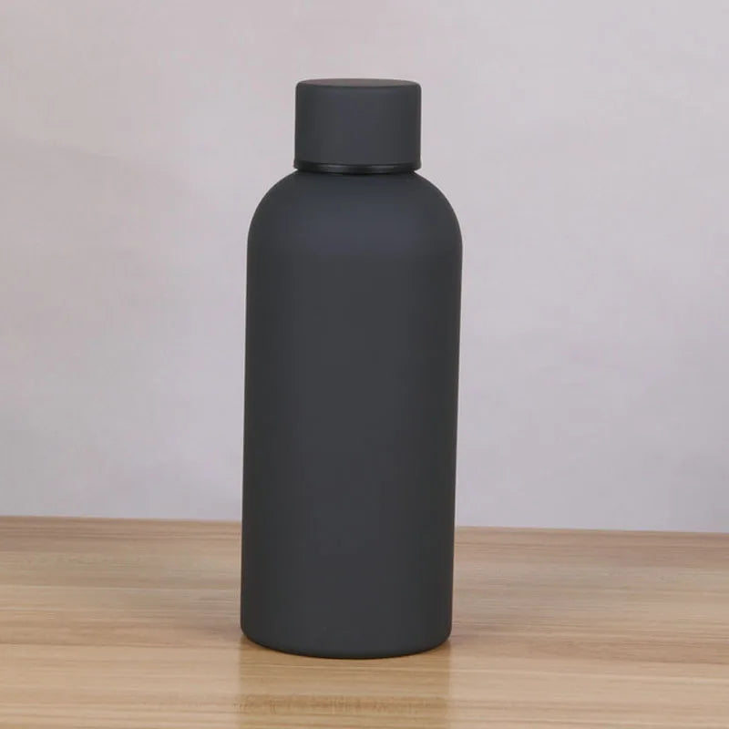 A matte dark gray double-layer vacuum thermos cup with a black cap sitting on a wooden surface.