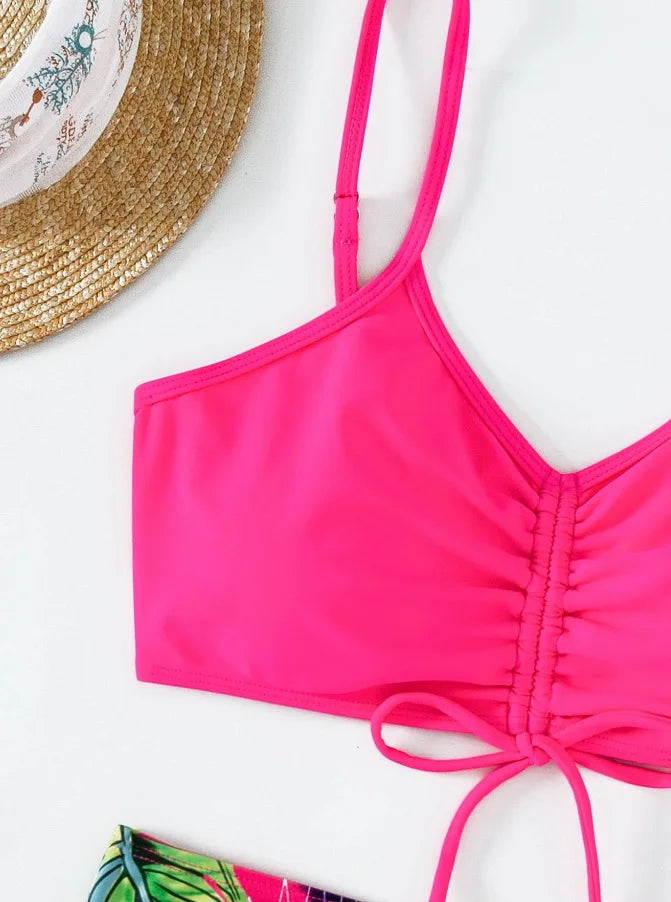 A bright pink two-piece bikini set with a tie-up top and bottoms is shown next to a straw hat.
