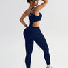 A woman wearing a navy blue seamless yoga jumpsuit with a cutout, posing against a light gray background.