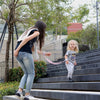 A young girl is walking down outdoor stairs while holding an adjustable child safety harness and leash.