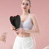 A woman holds a black pelvic floor muscle trainer device against her torso.