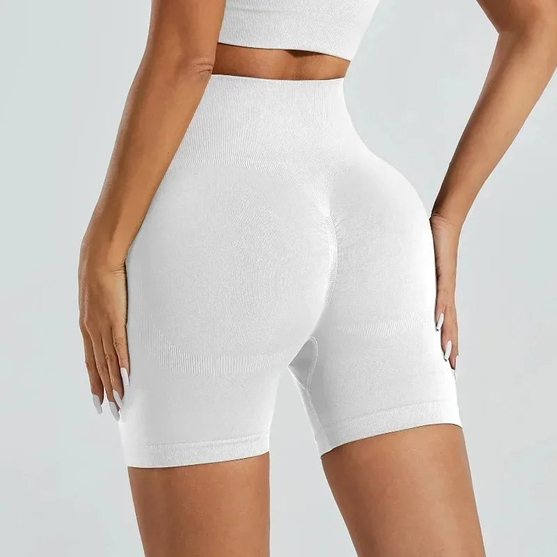 A model is wearing white high-waisted yoga shorts and a matching crop top.