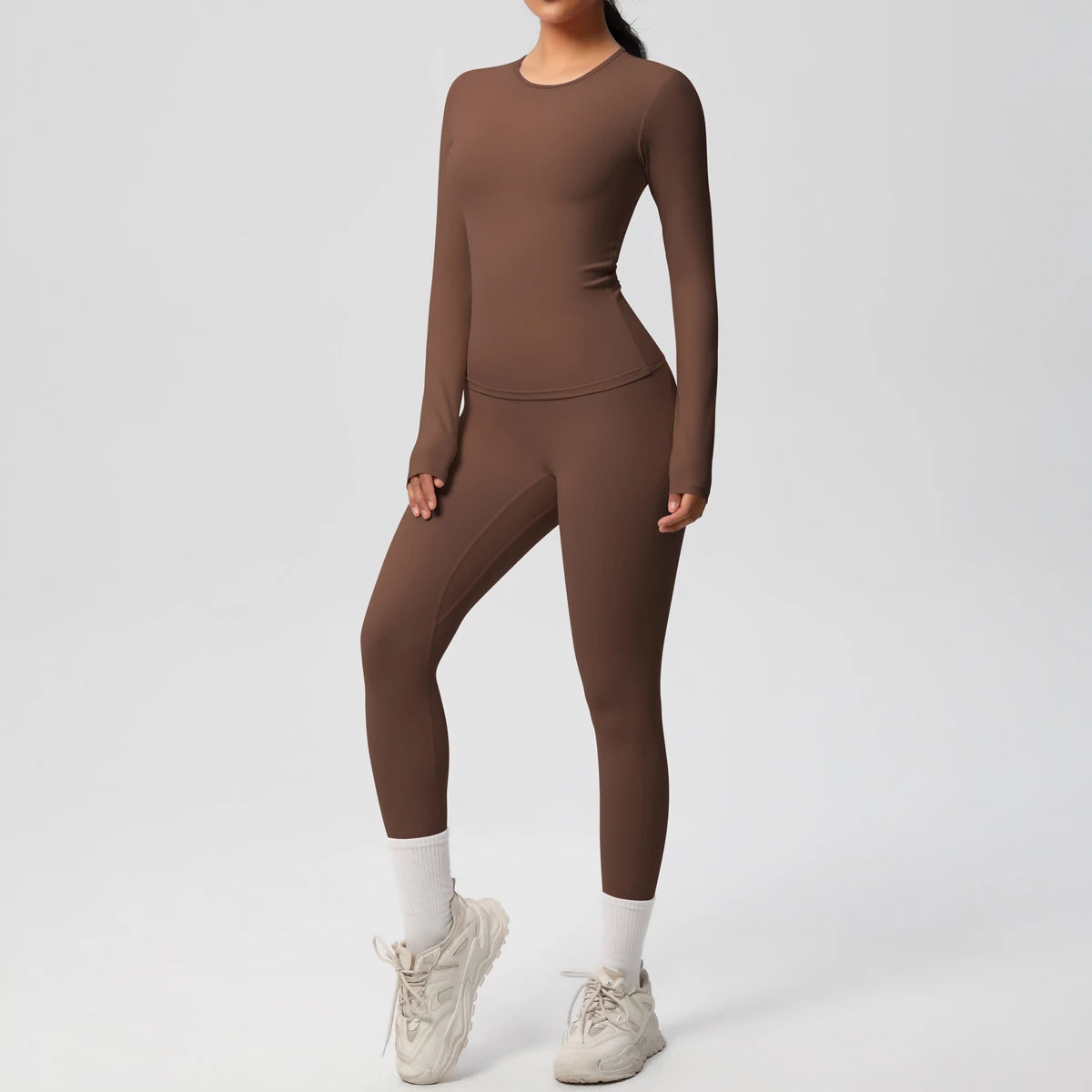 A woman wearing a long-sleeved brown performance yoga and gym set with white socks and light gray athletic shoes.