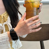 A person holds a glass of iced tea with a recipe on the side, next to a black silicone watch band.