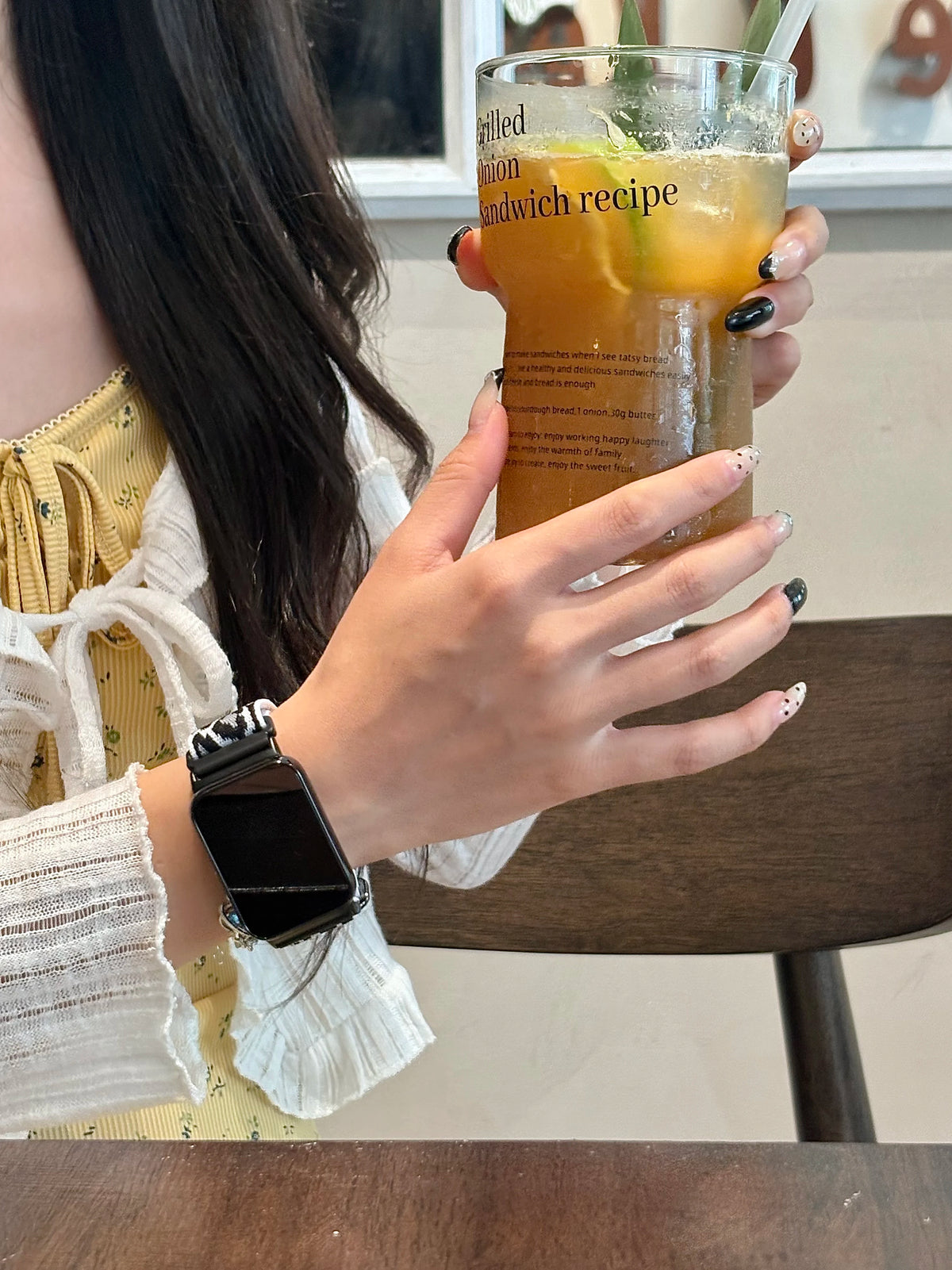 A person holds a glass of iced tea with a recipe on the side, next to a black silicone watch band.