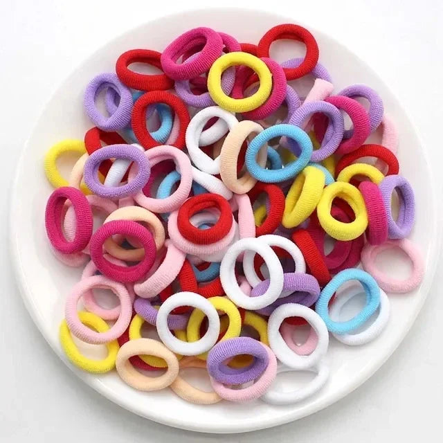Eine Ansammlung farbenfroher Nylon-Elasthebändchen in verschiedenen Rosa-, Gelb- und Violetttönen auf einem weißen Teller.