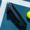 A black Owala insulated stainless steel travel mug resting on a blue surface next to a yellow tennis ball.
