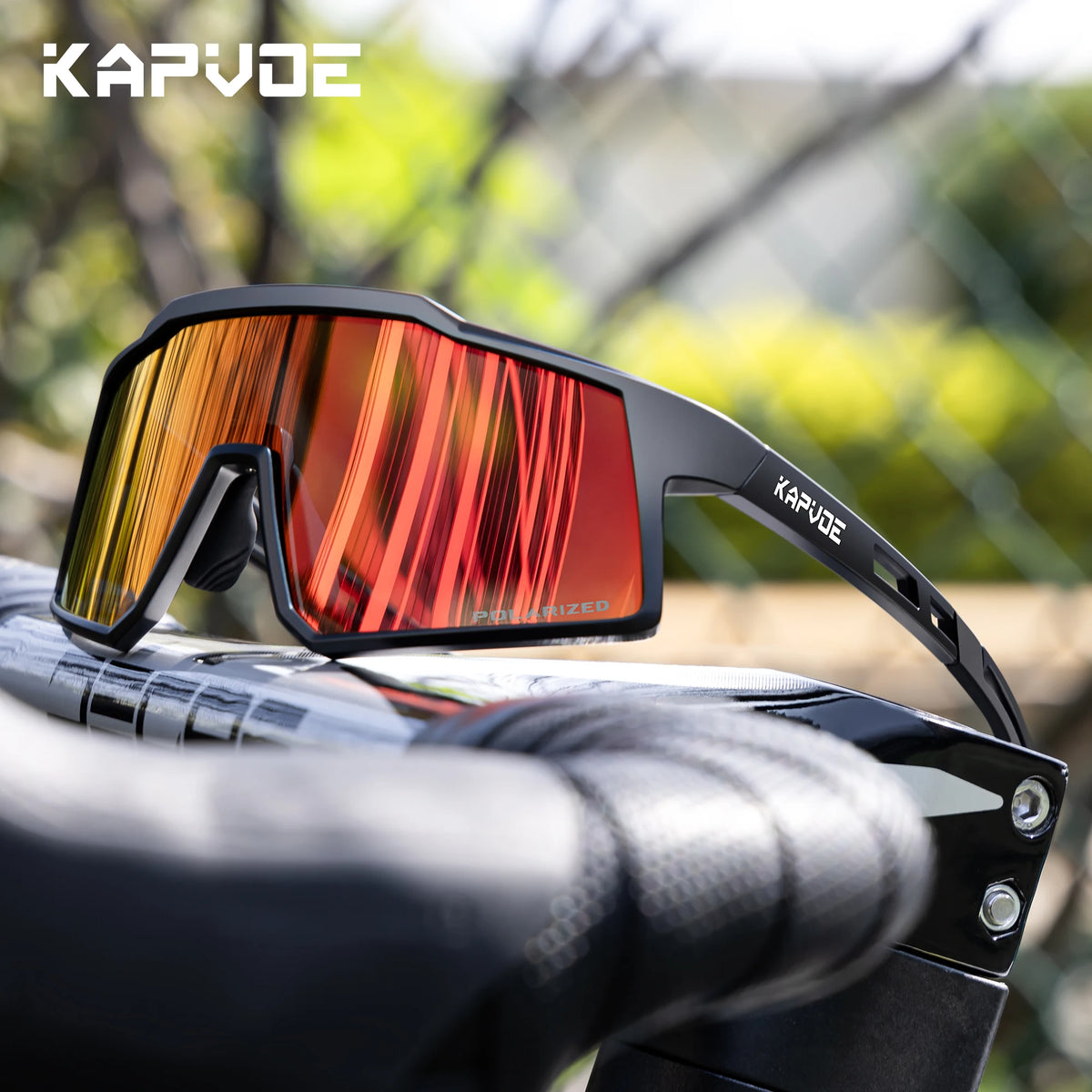 A pair of orange-tinted Kapvode polarized sports sunglasses resting on a black handlebar.