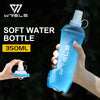 A hand holds a light blue soft water bottle with a clear cap against a dark background.
