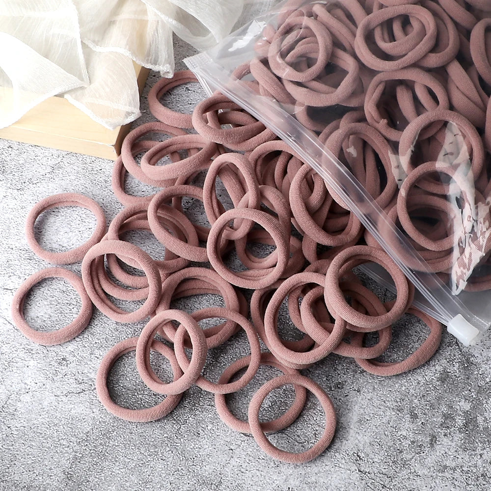 A pile of 50 pieces of mixed color elastic hair bands in a clear plastic bag on a gray surface.