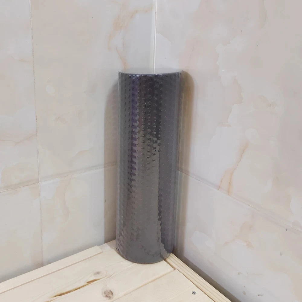 A gray hexagonal EVA foam yoga roller standing upright against a white tiled wall.