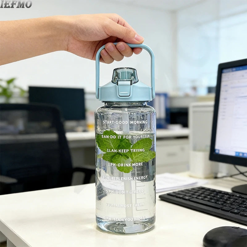 Eine Hand hält eine klare Wasserflasche mit blauem Deckel und Zeitmarkierungen auf einem weißen Schreibtisch.