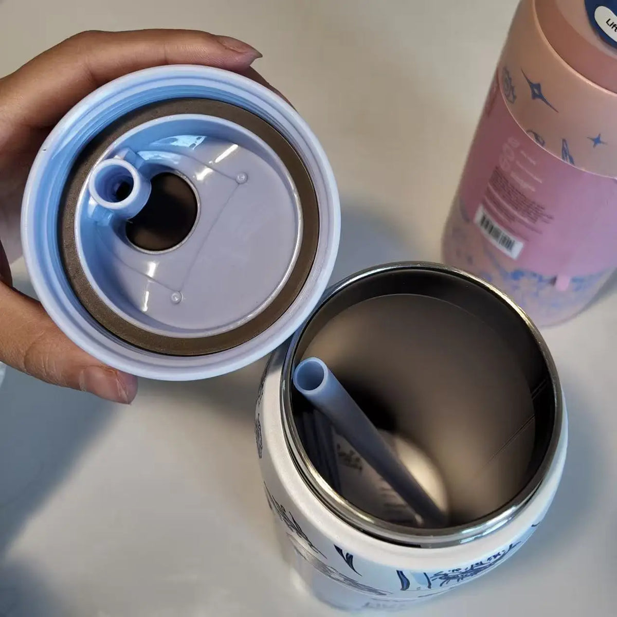 A hand holds a stainless steel vacuum insulated water bottle with a straw and its lid, showing the bottle's texture and desig