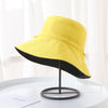 Yellow double-sided wide brim bucket hat displayed on a black stand.
