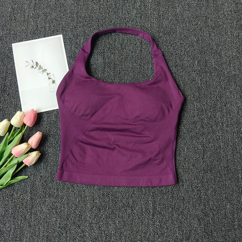 A deep purple seamless yoga and pilates sports bra laid on a dark gray textured surface with a white card and pink tulips.