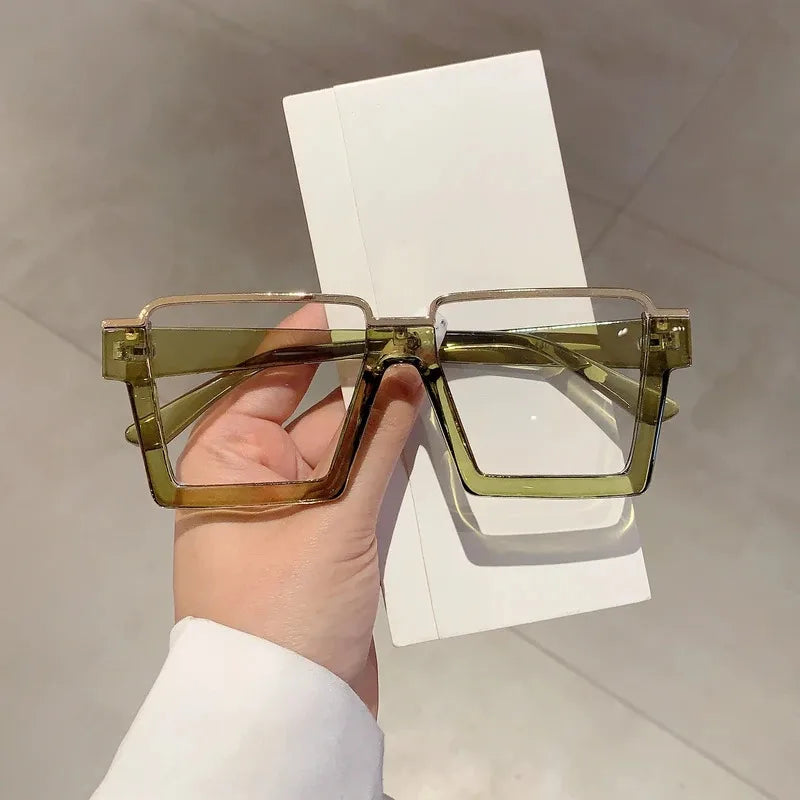 A pair of oversized square semi-rim metal eyeglasses with light green tinted lenses resting on a white card.