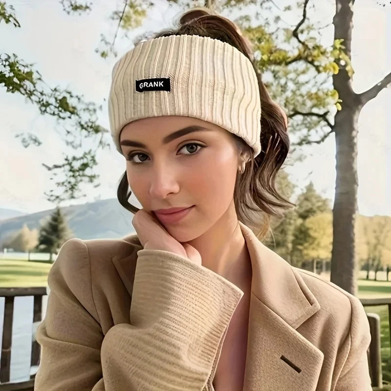 A woman wearing a beige knitted headband while posing outdoors.