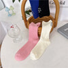 A set of elegant embroidered cotton socks in purple, black, and pink are displayed next to a woven basket.
