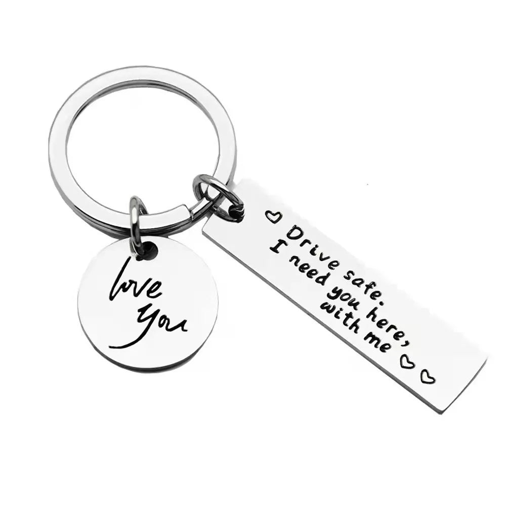 A silver metal keychain with a circular ring attached and a rectangular tag engraved with the words I love you Drive safe I n