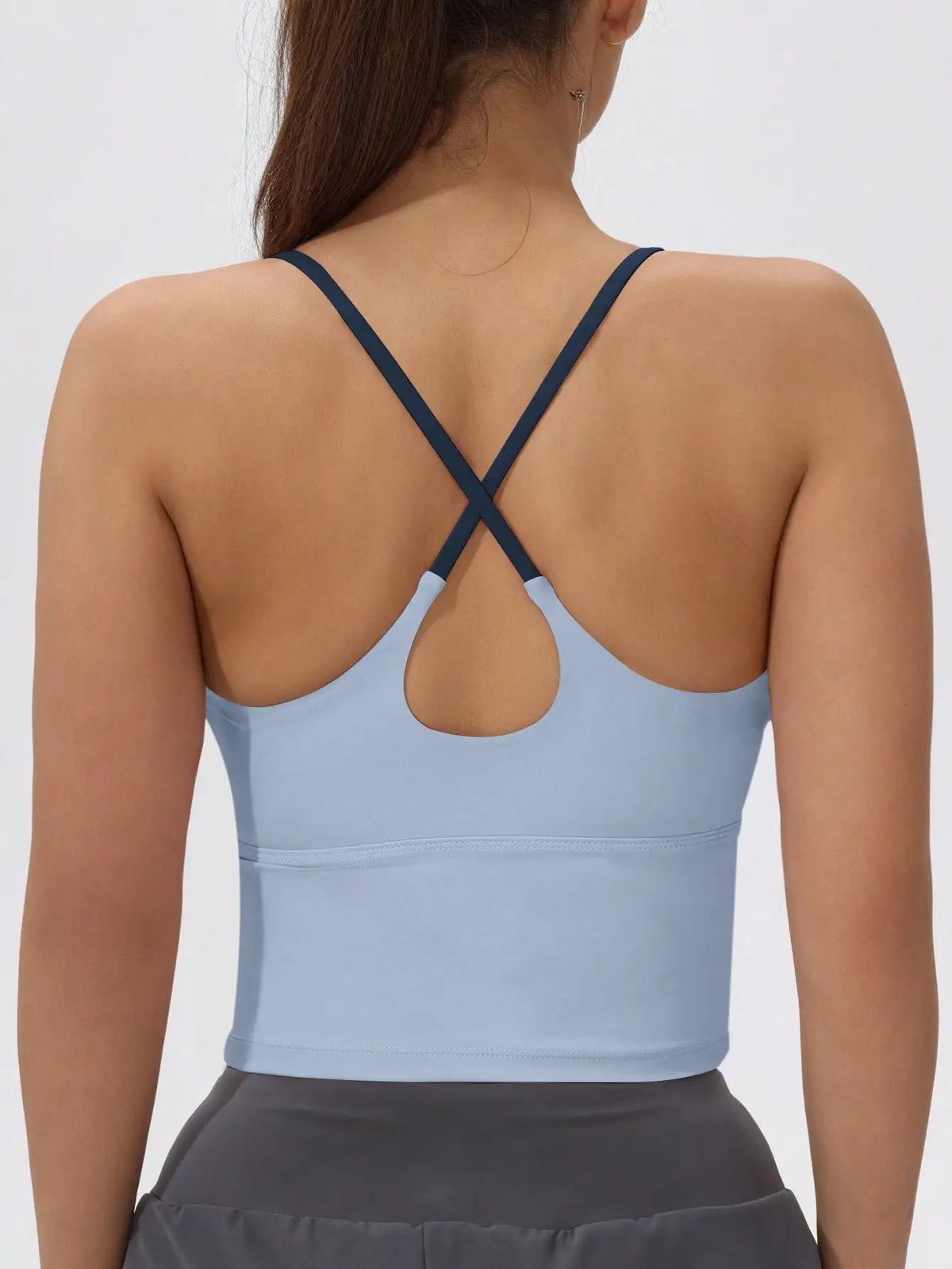 A woman wearing a light blue athletic crisscross tank top with a gray skirt.