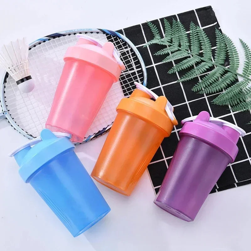 A collection of colorful portable protein shaker bottles in pink, orange, blue, and purple are displayed on a mesh background