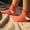 A pair of coral knit socks with crocodile ears resting on a fluffy white blanket.