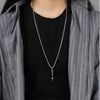 A stainless steel whistle pendant necklace worn by a person under a gray striped jacket and black shirt.