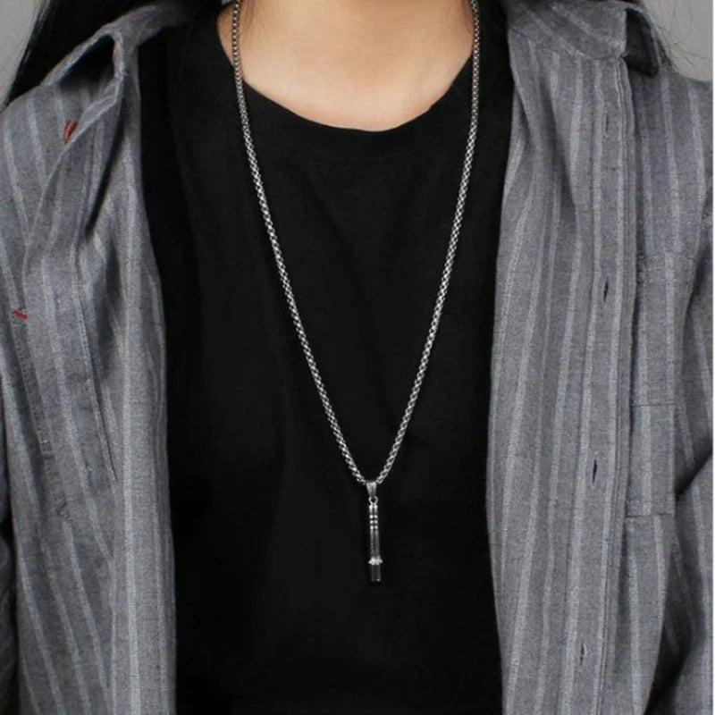 A stainless steel whistle pendant necklace worn by a person under a gray striped jacket and black shirt.