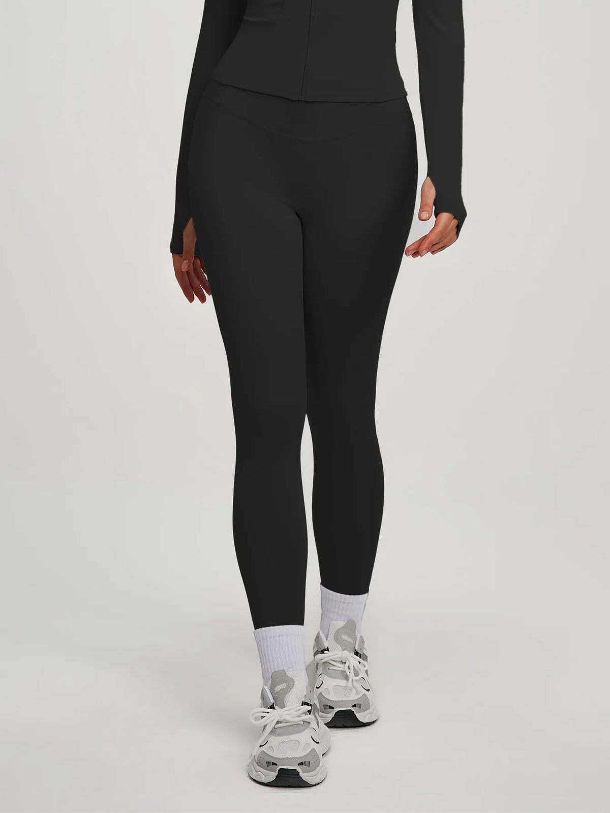 Eine Frau trägt ein schwarzes Yoga-Sportset mit langärmeligem Oberteil und Leggings.