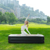 A woman lying on a black air mattress outdoors with a city skyline in the background.