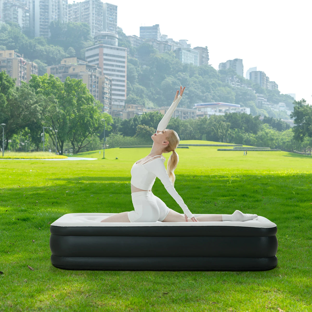 A woman lying on a black air mattress outdoors with a city skyline in the background.