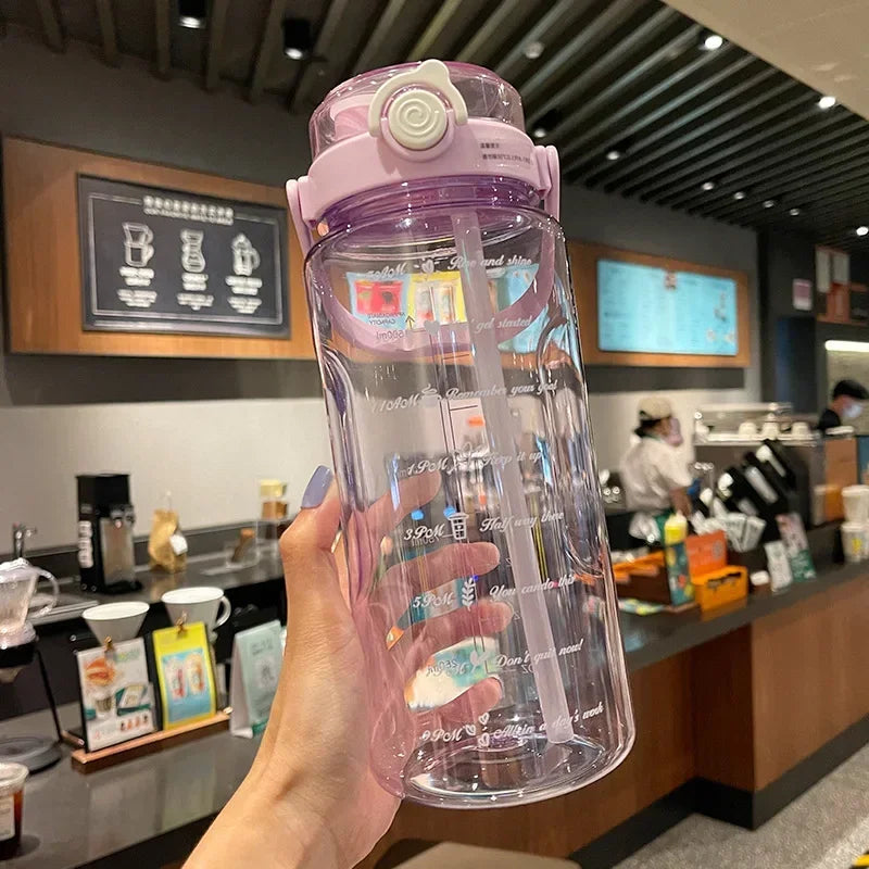 A hand holds a clear purple water bottle with a straw and time scale markings in a cafe setting.