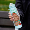 A hand holds a light blue water bottle featuring a cute brown capybara design with a strawberry and a green straw.